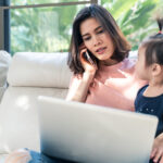 Woman working on laptop while on phone with child