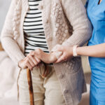 Caregiver helping an elderly woman walk with a cane